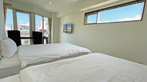 Une chambre d’hôtel avec deux lits, un téléviseur fixé au mur et de grandes fenêtres donnant sur le paysage urbain.