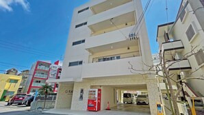 Un immeuble à plusieurs étages, doté d’une architecture moderne, avec des balcons aux étages supérieurs et une entrée au niveau du sol.