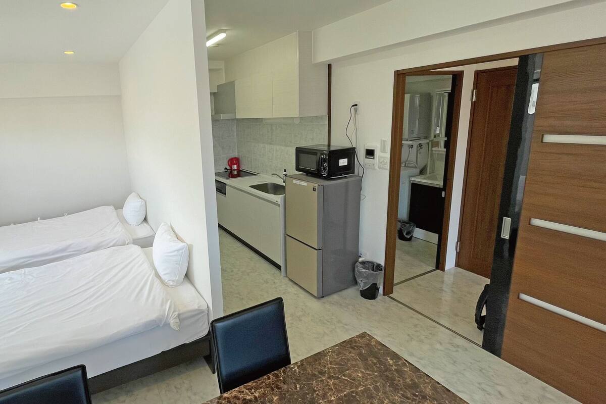 A compact hotel room with a bed, a small table, and a kitchenette.