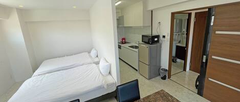 A compact hotel room with a bed, a small table, and a kitchenette.