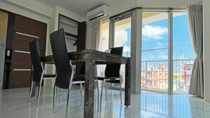 Une chambre moderne équipée d’une table à manger, de chaises et d’une grande porte-fenêtre coulissante donnant sur un balcon avec vue sur la ville.