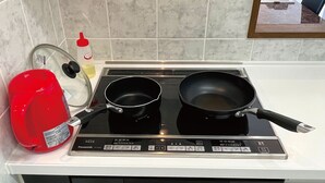 Une cuisine équipée d’une cuisinière, de deux casseroles, d’une bouilloire rouge et d’une bouteille d’huile.