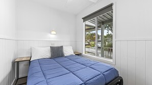 Ein Schlafzimmer mit Bett, Nachttisch, Lampe und Fenster mit Blick nach draußen.