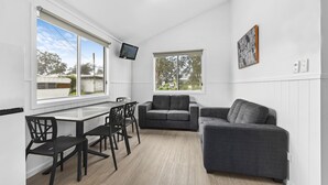 Ein modernes Wohnzimmer mit Essbereich, großen Fenstern, einem Flachbildfernseher und einem grauen Sofa.