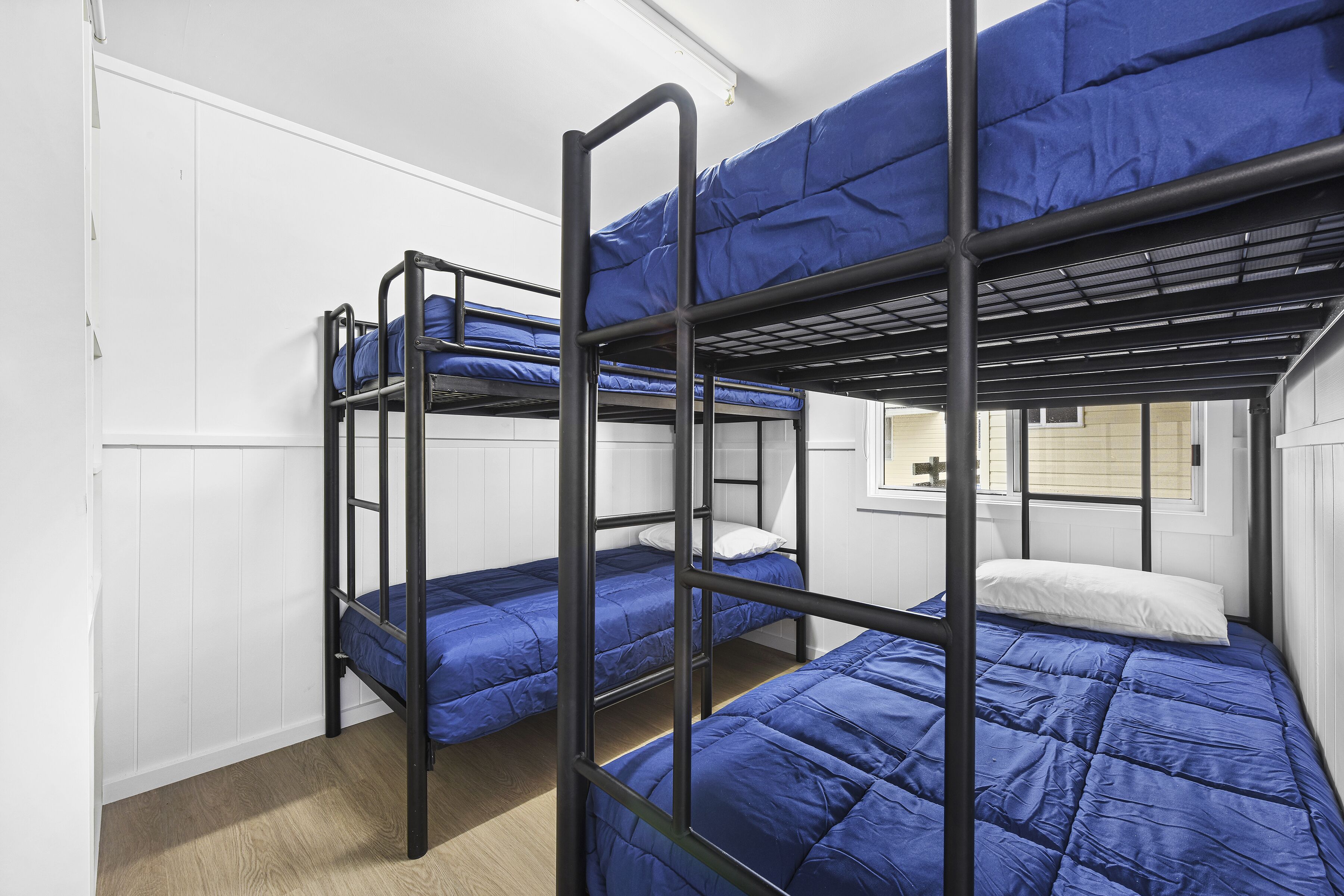 A dormitory room with bunk beds, white walls, and a window.