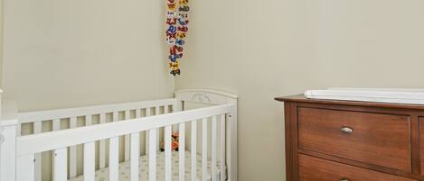 A white crib with a patterned mattress, a wooden dresser with drawers, and a wall-mounted decoration.
