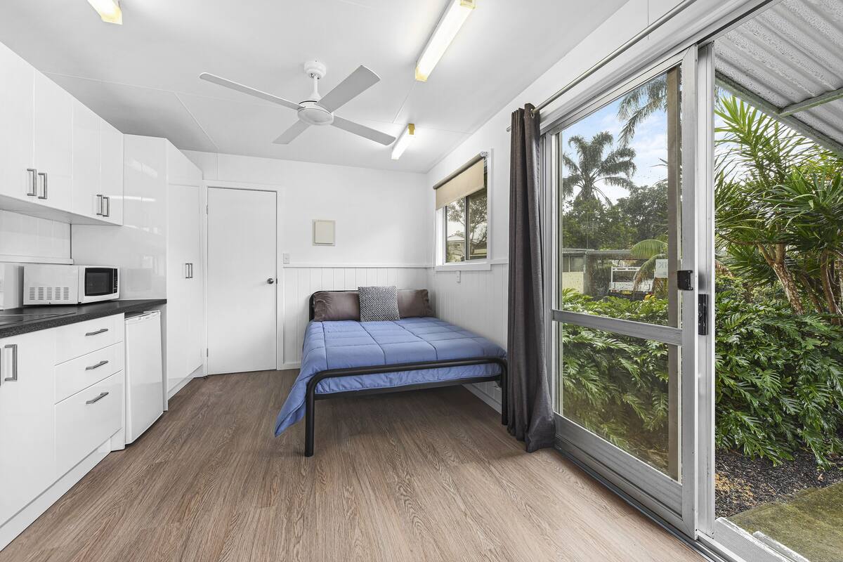 A compact room with a bed, kitchenette, and large sliding glass door to a garden.