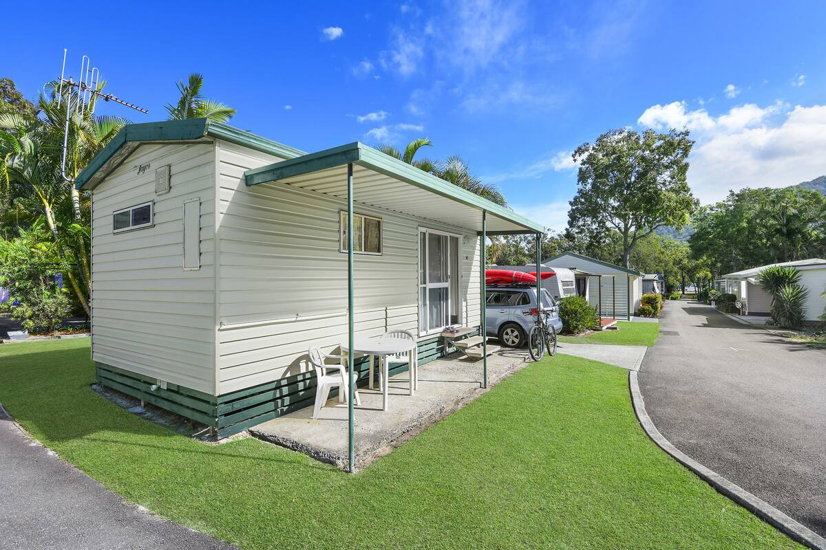 A single-story mobile home with a green roof, a covered porch, and a small patio area with a table and chairs.