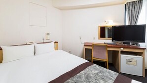 A hotel room with a bed, a desk with a computer, a chair, and a small refrigerator. - Pearlhotel Kawasaki (Kawasaki)