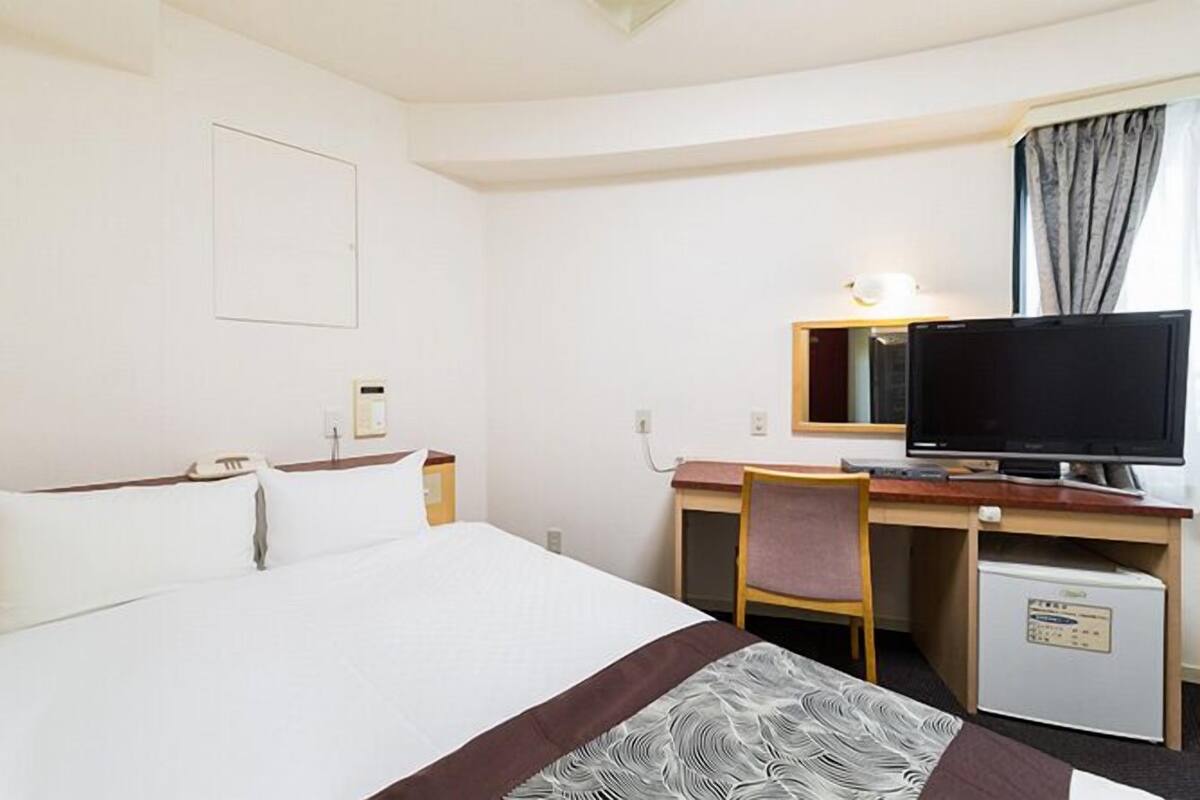 A hotel room with a bed, a desk with a computer, a chair, and a small refrigerator.