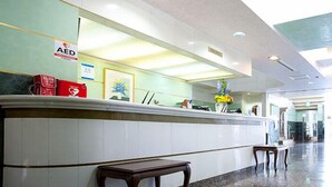 A clean, well-lit lobby with a reception desk, AED sign, and a vase with flowers. - Pearlhotel Kawasaki (Kawasaki)