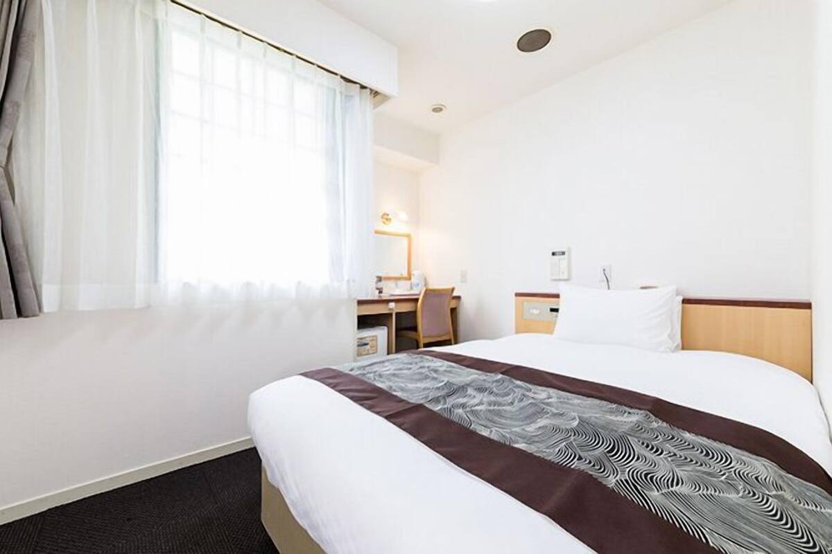 A hotel room with a large bed, a desk, and a chair.