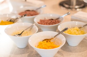 Een buffettafel met verschillende witte kommen vol met diverse soorten eten.