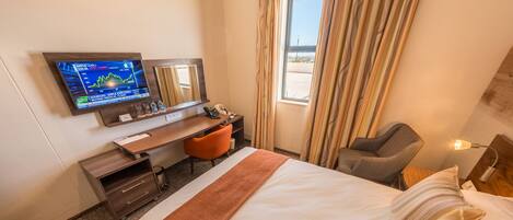 A hotel room with a bed, desk, chair, TV, and window with curtains.