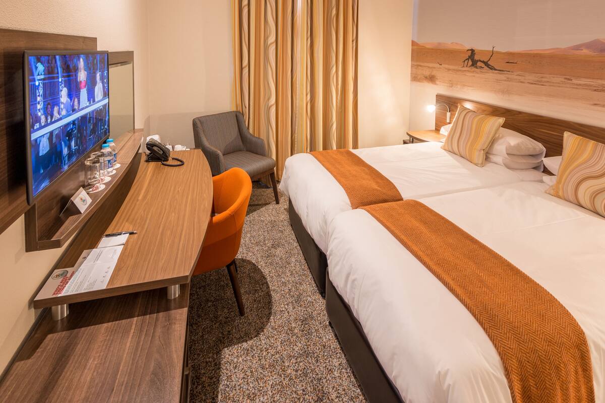 A hotel room with a bed, a desk, a chair, a TV, and a curtain.