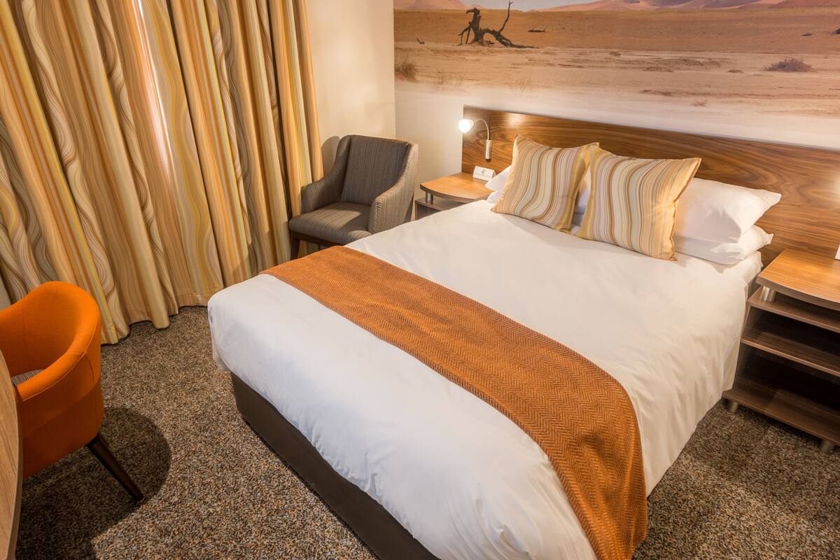 A hotel room with a large bed, a chair, a nightstand, and a wall mural.