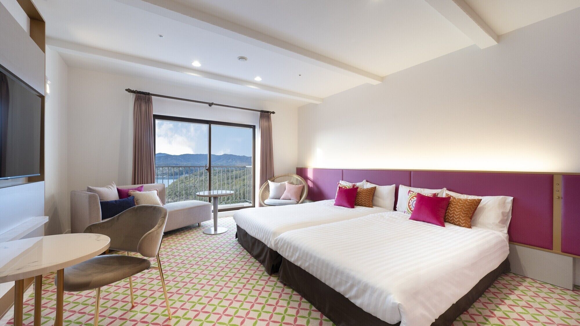 Quarto de hotel com cama grande, sofá, poltrona, mesinha e varanda com vista.