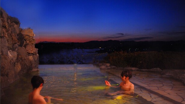 Uma piscina de pedra com vista para um pôr do sol sobre uma paisagem montanhosa.