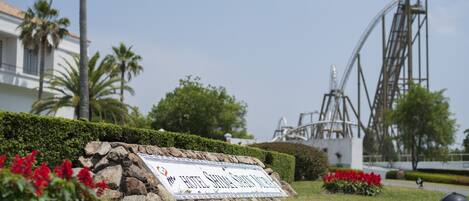 A sign for Hotel Stella Maris in a landscaped area with a roller coaster in the background.