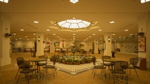 Um hall amplo com uma fonte central, diversas áreas de estar e um teto alto com claraboia.