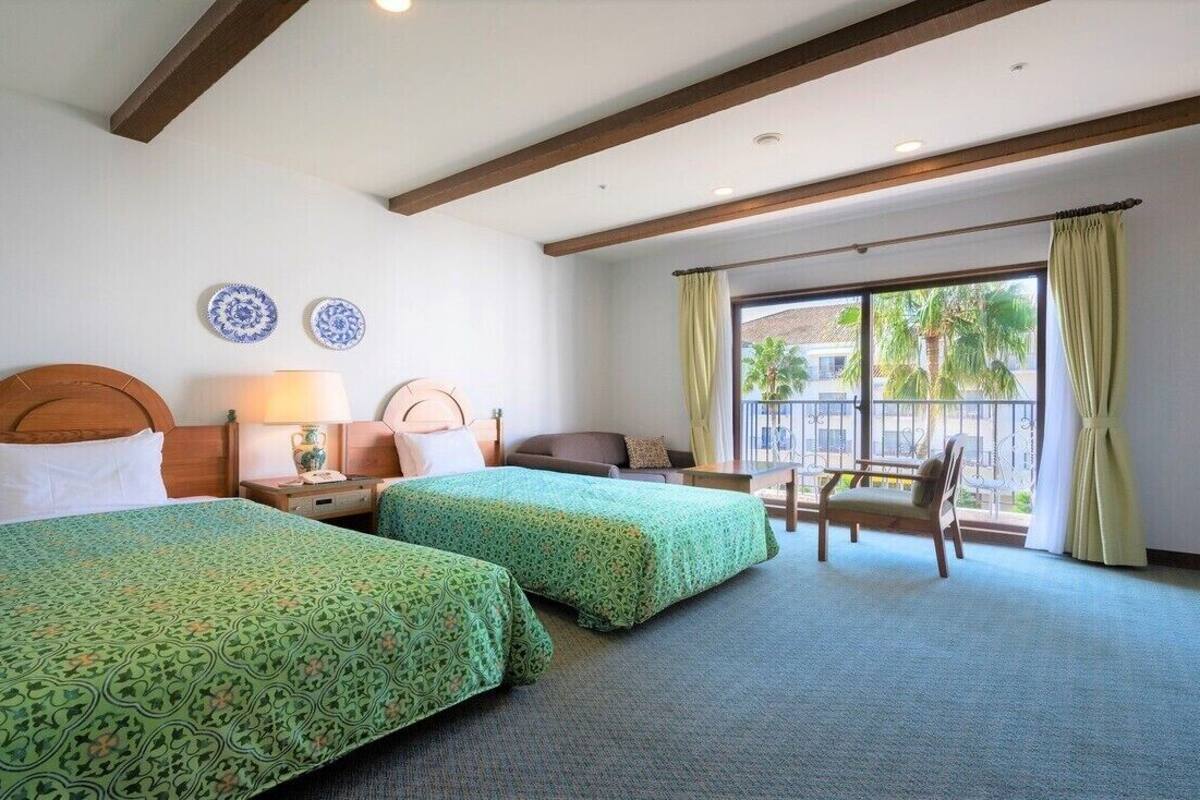 Een hotelkamer met twee bedden, een stoel, een tafel en een raam met gordijnen.