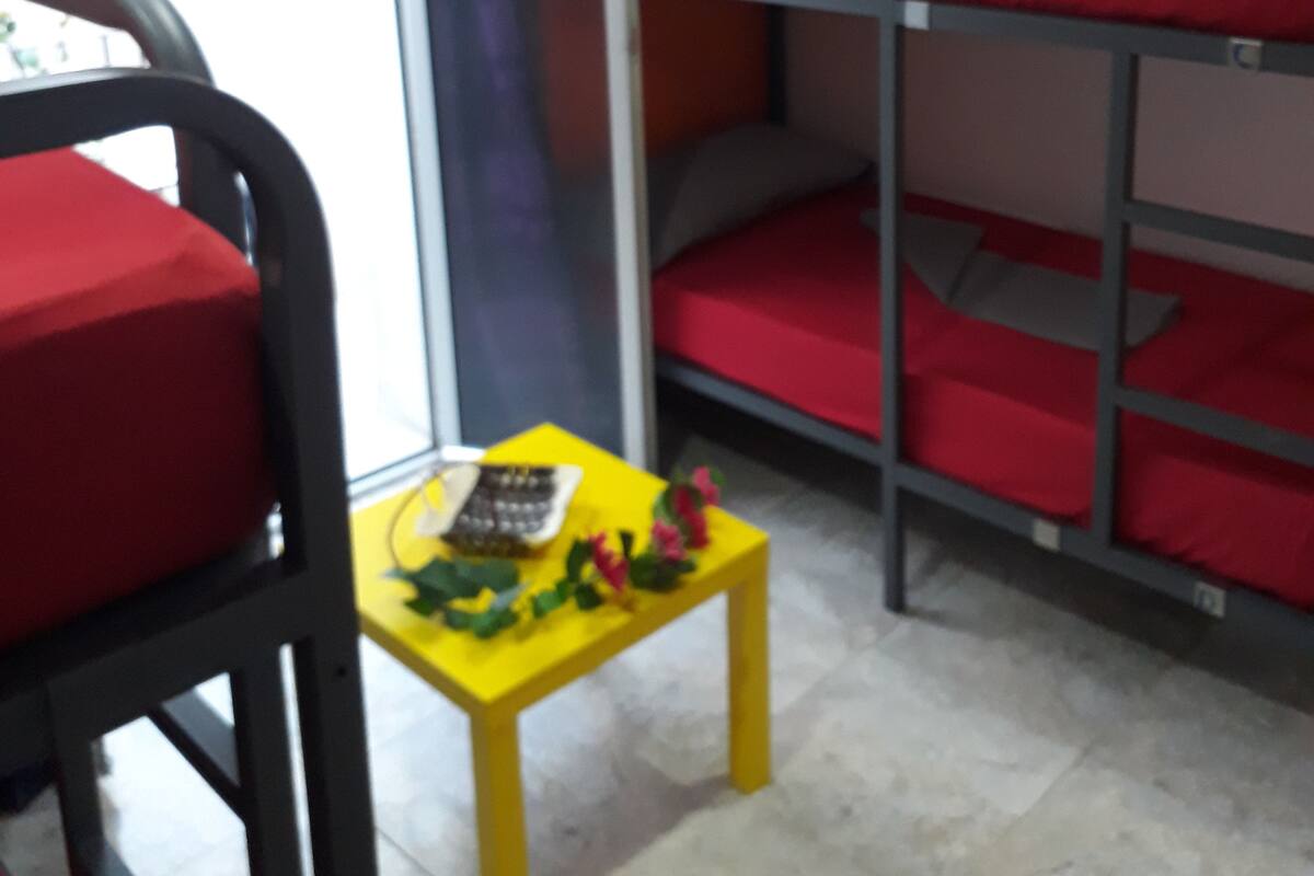 A dormitory room with bunk beds, a small table with toys, and a window with curtains.
