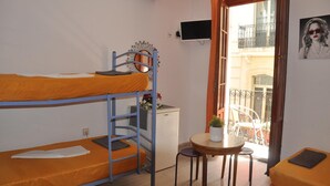 A dormitory room with bunk beds, a small desk, a chair, a potted plant, and a balcony with a view. - Hostal Mayor (Alicante)