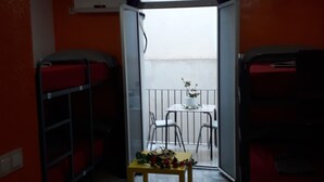 A room with bunk beds, a small table with flowers, and a balcony with chairs. - Hostal Mayor (Alicante)