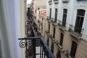 A narrow street with buildings on either side, featuring balconies with wrought iron railings and a mix of architectural styles. - Hostal Mayor (Alicante)