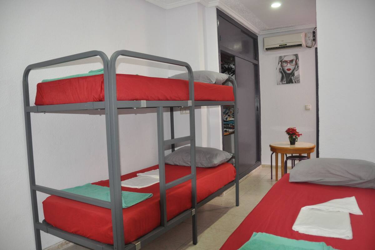 A bunk bed room with a red mattress, a small table with a vase, and a poster on the wall.