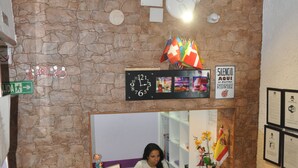 A reception area with a stone wall, a clock, a framed photo, and a sign indicating silence. - Hostal Mayor (Alicante)
