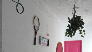 A room with a bed, a pink door, a tennis racket, and a hanging plant. - Hostal Mayor (Alicante)
