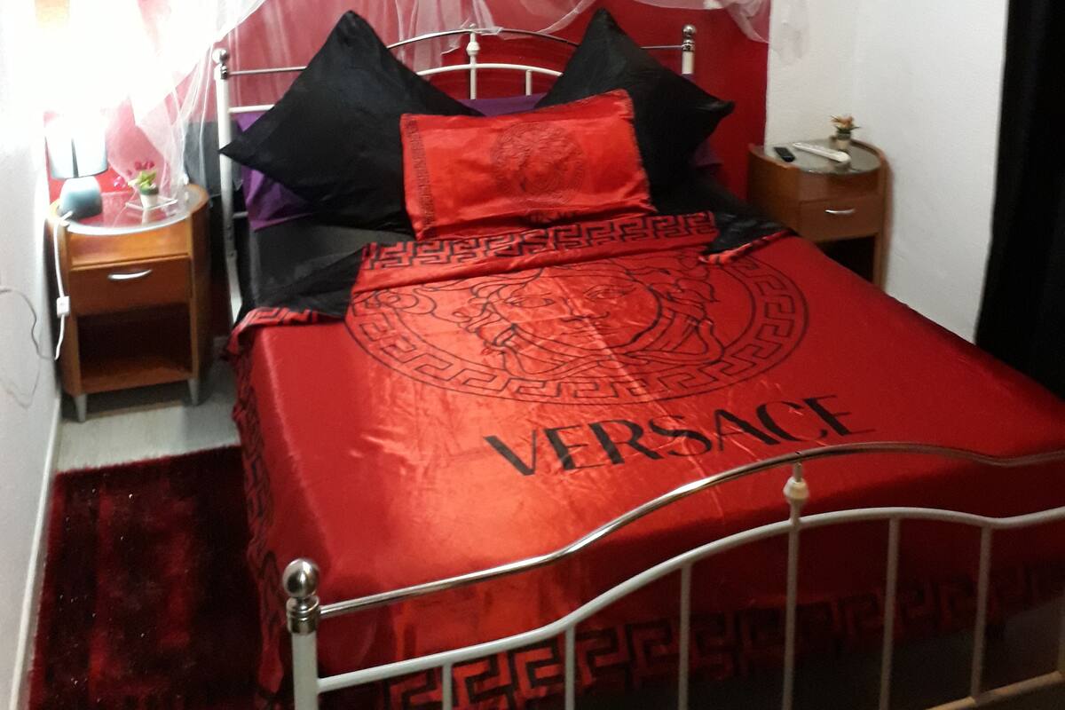 A bed with a red Versace bedspread, a white canopy, and black and red pillows.