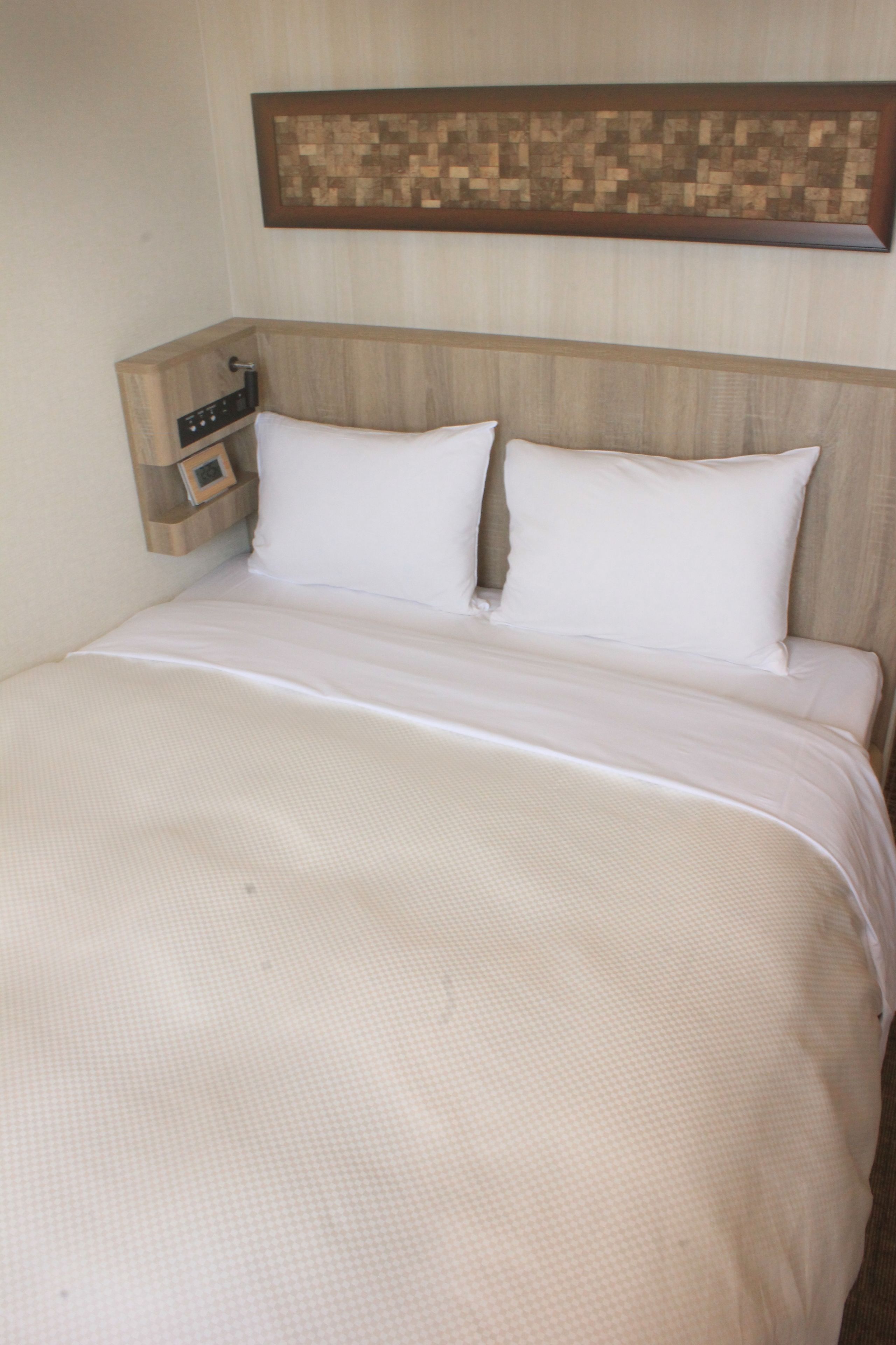 A neatly made bed with a wooden headboard and a small bedside table with a clock.