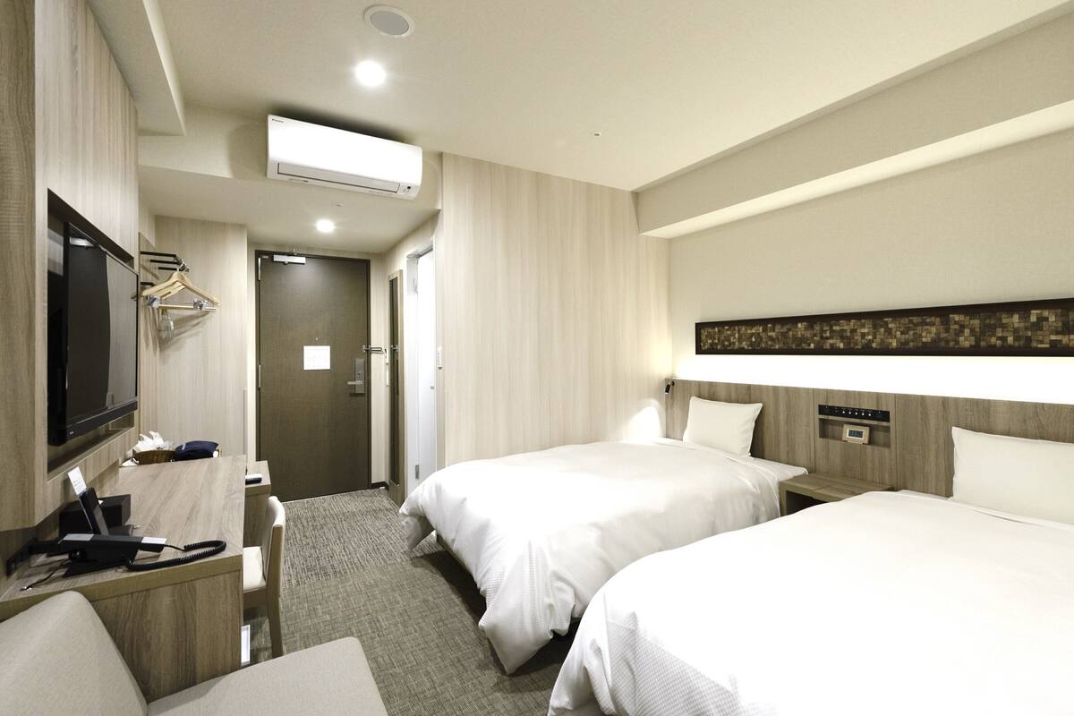 Quarto de hotel com duas camas, uma mesa de escritório com telefone, TV e ar condicionado.