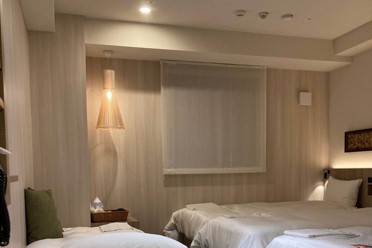 Quarto de hotel com duas camas, uma mesa de cabeceira, um abajur e uma televisão fixada na parede.