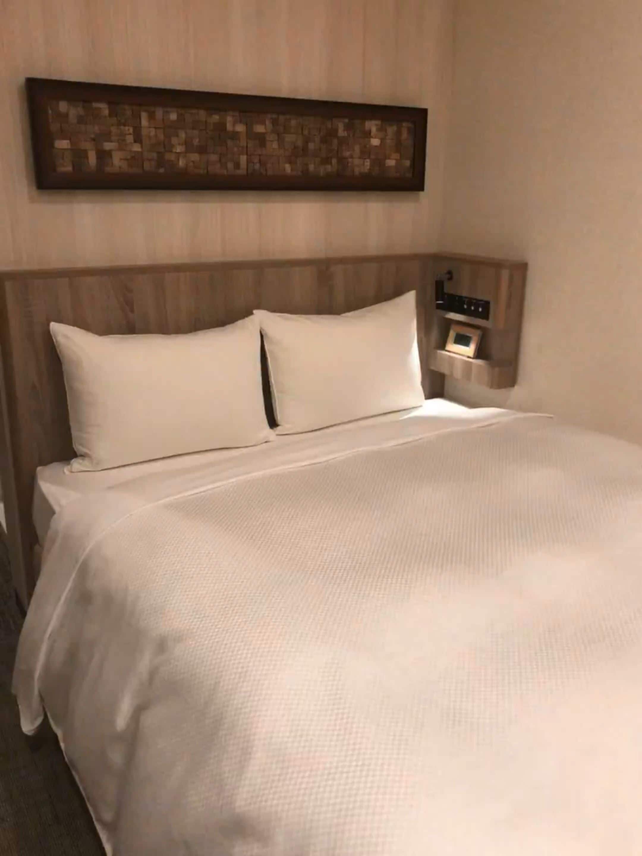 A neatly made bed with a large pillow and a headboard with a built-in nightstand.