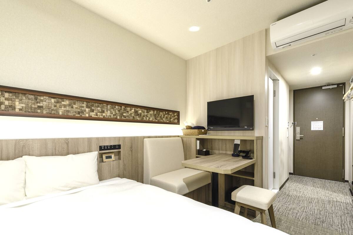 Quarto de hotel com cama, escrivaninha, cadeira, televisão e ar condicionado.