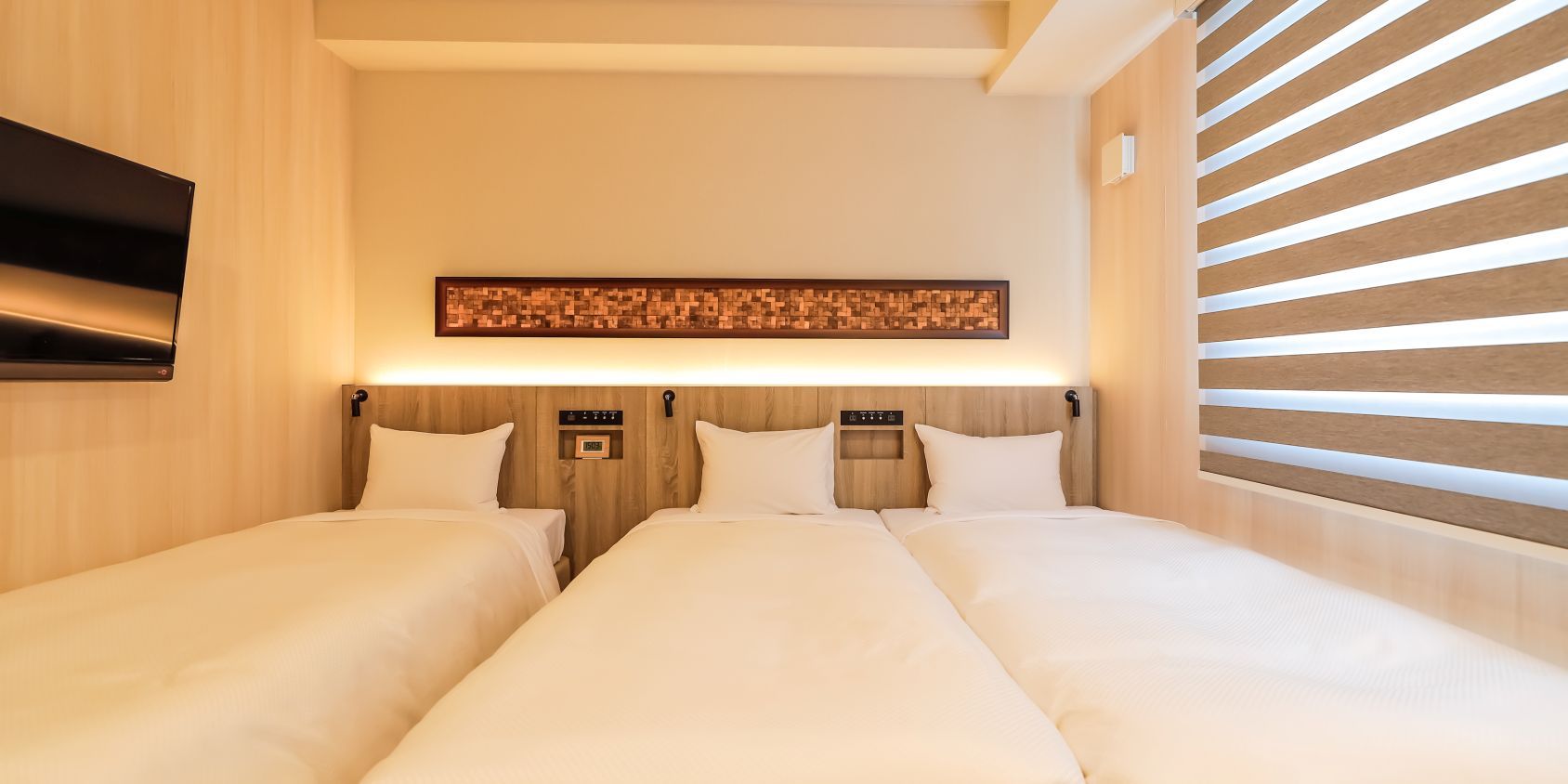 A hotel room with two beds, a flat-screen TV mounted on the wall, and a wooden headboard with a decorative panel above.