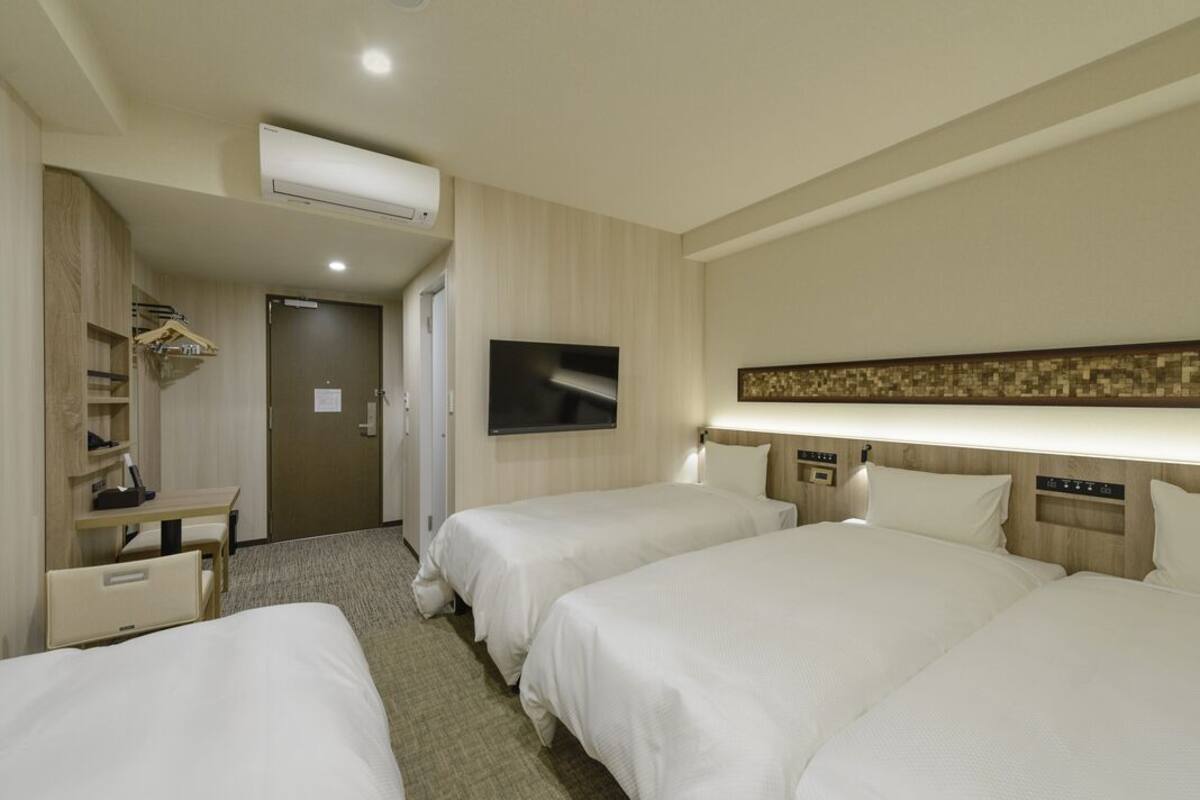 Quarto de hotel com duas camas, uma escrivaninha, televisão e guarda-roupa.