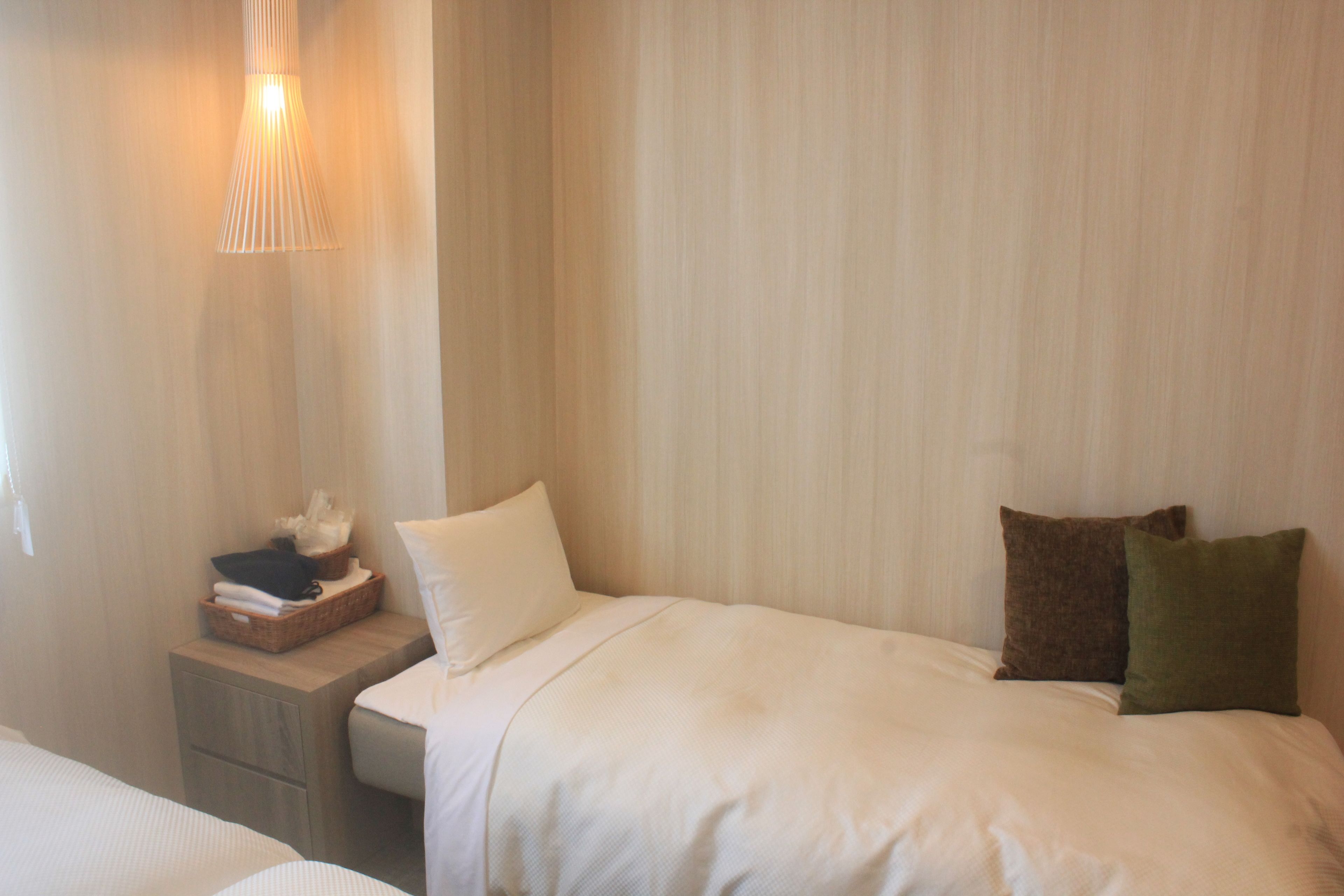 Habitación de hotel con cama, mesita de noche, lámpara y repisa con artículos de aseo.