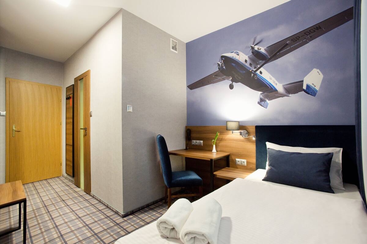 A hotel room with a bed, a desk, a chair, and a wall mural of an airplane.