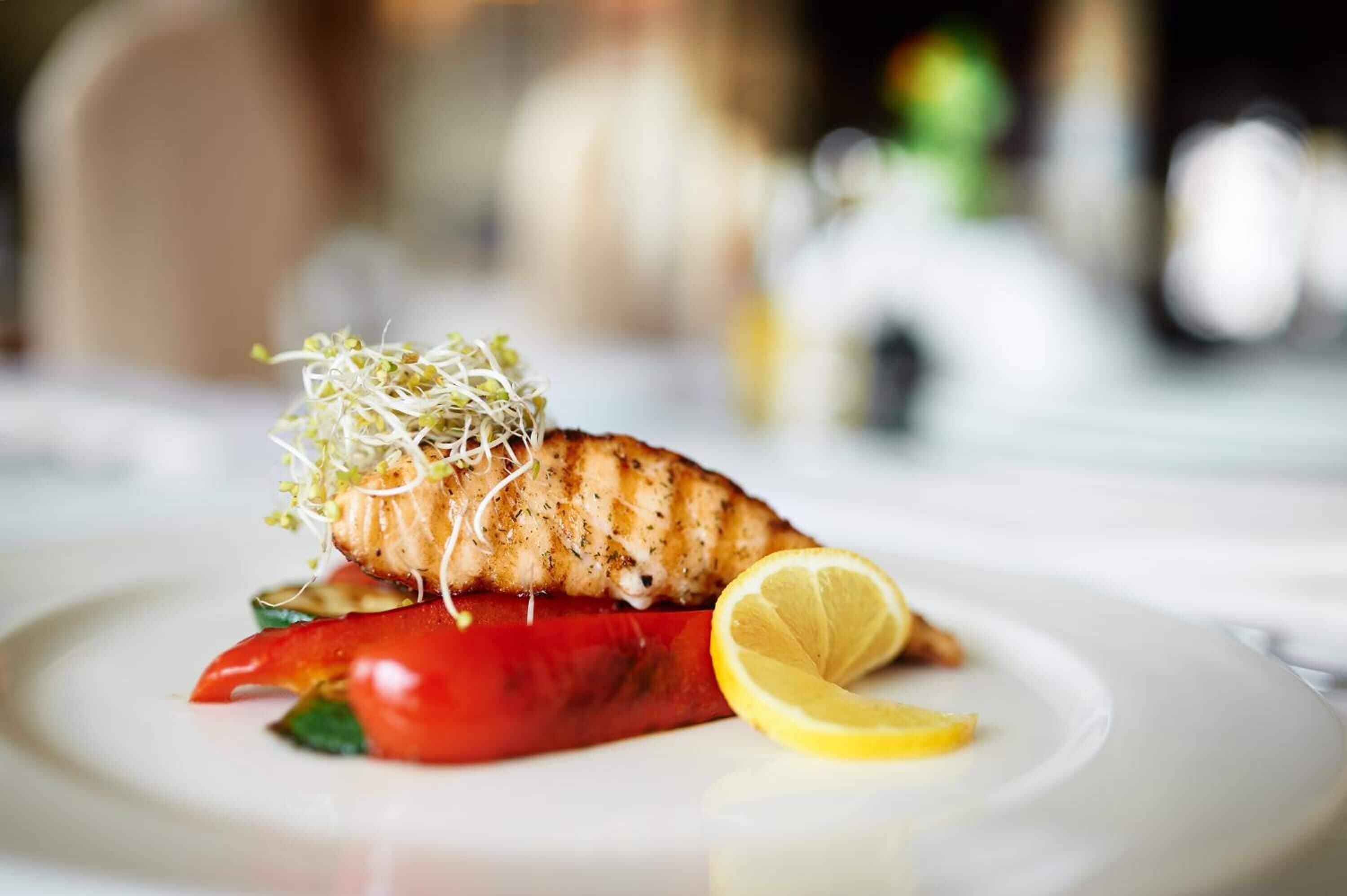 A plate with grilled salmon, sprouts, a slice of red pepper, and a lemon wedge.