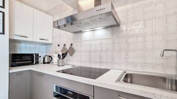 A modern kitchen with white cabinets, a stainless steel range hood, a microwave, a kettle, and a sink.