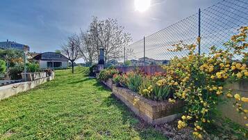 A grassy area with a concrete planter, a metal fence, and a building in the background.