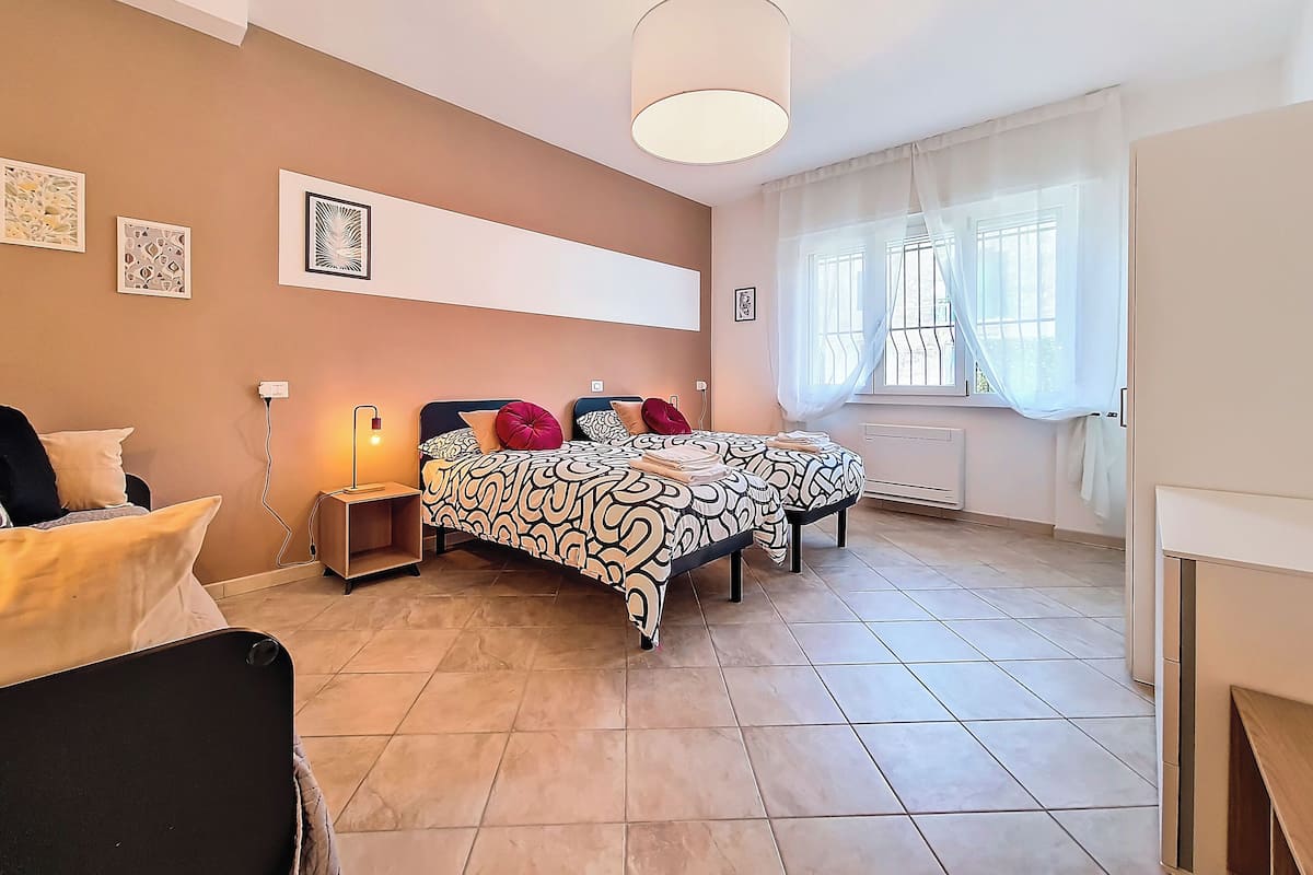 A bedroom with two beds, a bedside table, a lamp, and a window with curtains.