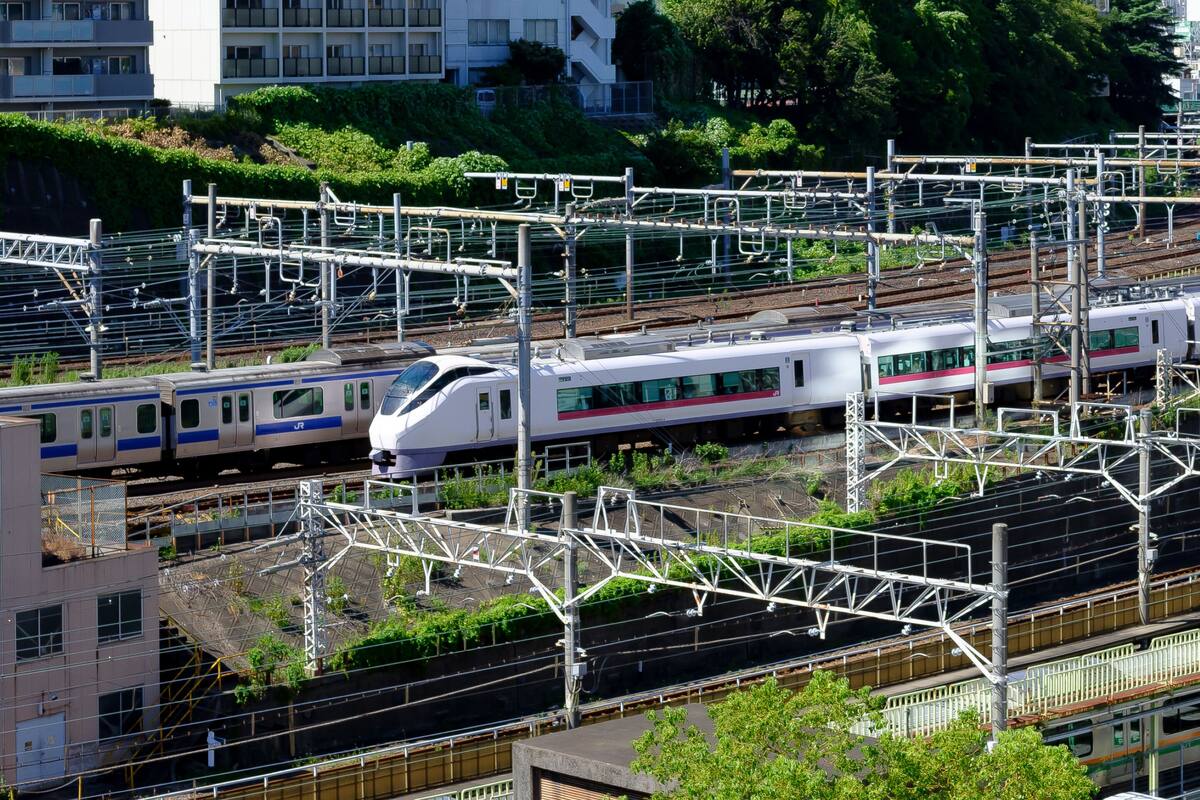 A high-speed train passing through an urban area with multiple tracks and overhead electrical lines.