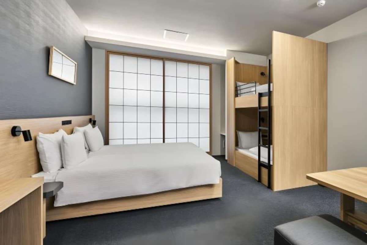 A modern hotel room with a large bed, a bunk bed, a desk, and a sliding door closet.