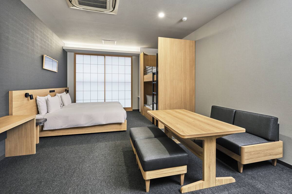 A modern hotel room with a bed, a desk, a table, and a bench.