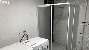 Uma lavanderia com máquina de lavar e secadora, box de chuveiro e estante de metal.
